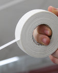 Hand holding a roll of white tape against a neutral background