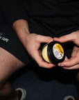 Person holding a jar of cream with a brand logo, sitting on a dark surface.