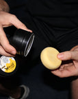 Person holding a can of spray paint and a yellow sponge against a dark background