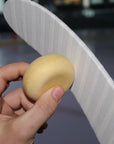 Hand holding a potato near a white curved object with a blurred background