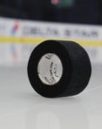 Roll of black tape with a label on a white surface, with a blurred background.
