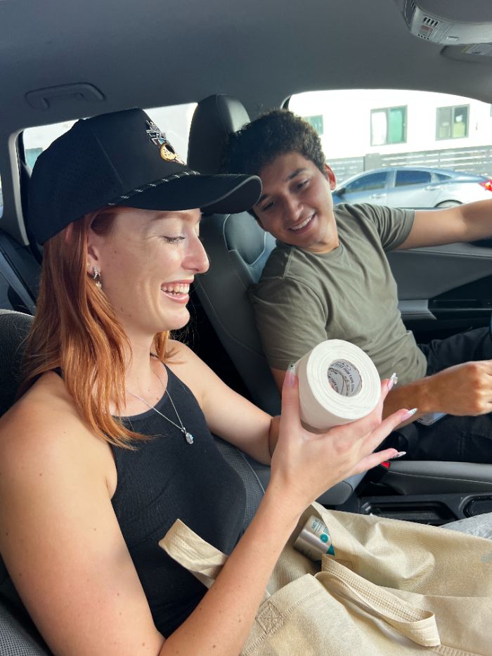 Two friends in a car smiling at a roll of Best Dam Tape